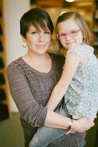 A woman holding her young daughter as both smile facing forward