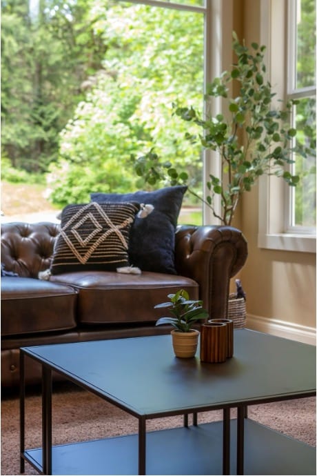A sofa and coffee table in a room with large, open windows; one of Mission Connection’s facilities.