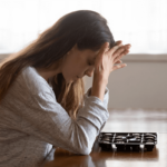 Young woman with long hair sitting at table with head in hands experiencing anxiety