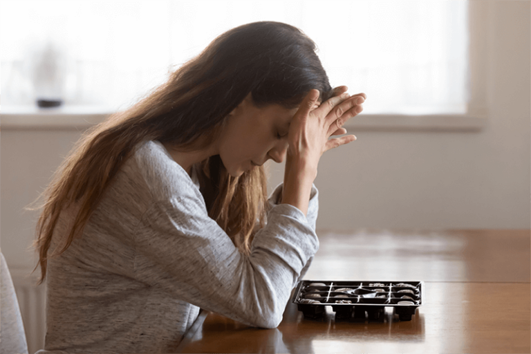 Young woman with long hair sitting at table with head in hands experiencing anxiety