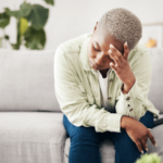 Woman on couch bent forward with elbows on knees holding head in hand