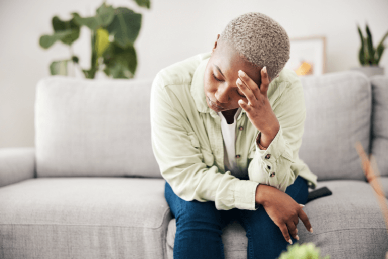 Woman on couch bent forward with elbows on knees holding head in hand