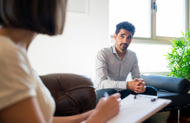 Man sitting on couch across from female psychologist who is taking notes during session
