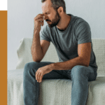 man sitting on couch, scrunching his face up and pinching his nose, in need of treatment for panic disorder