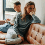 man on his phone while sitting on the couch with his girlfriend who is looking away, demonstrating avoidant attachment style