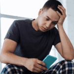 man looking at phone, wondering why he's experiencing avoidant ghosting again from a potential date