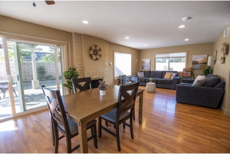 A peaceful therapy room at Mission Connection in an open living and dining area with wooden floors, a dining table, sliding glass doors, and a seating area with dark sofas and modern decor.