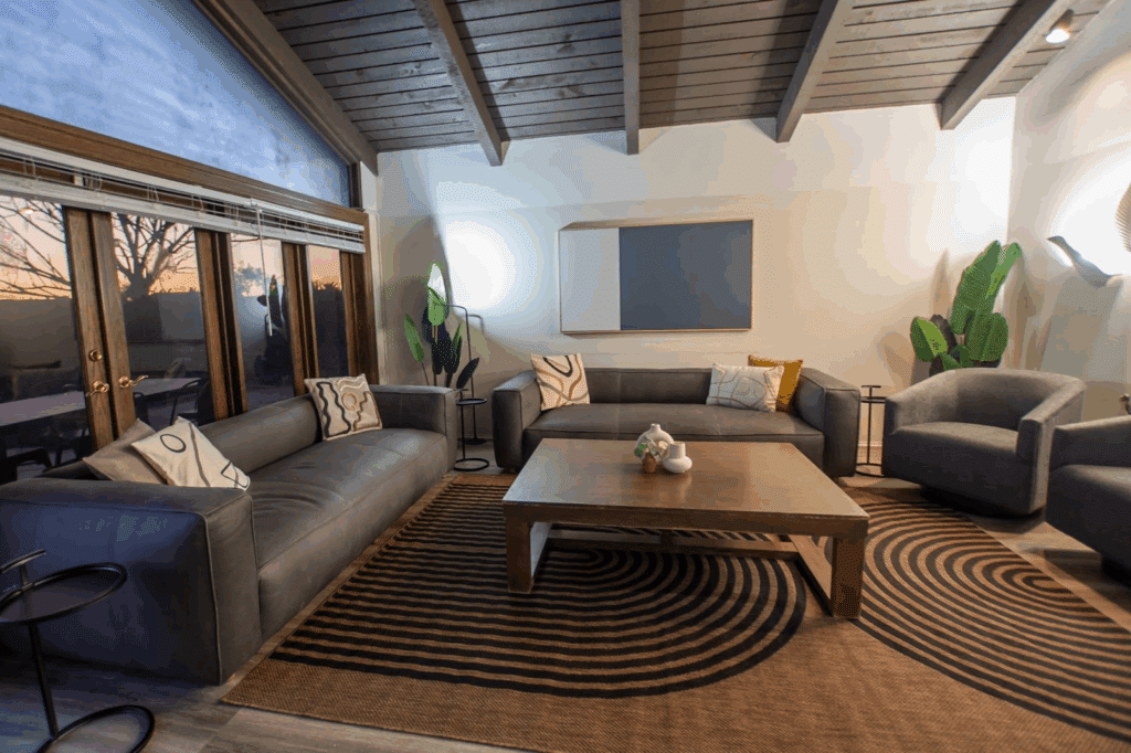 A welcoming group therapy room at Mission Connection with two gray sofas, two armchairs, a wooden coffee table, patterned rug, and potted plants for decoration.