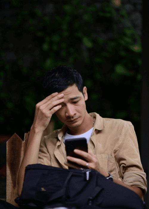 Man using phone in natural setting while holding his hand on his head due to physical & stress-related symptoms in adults
