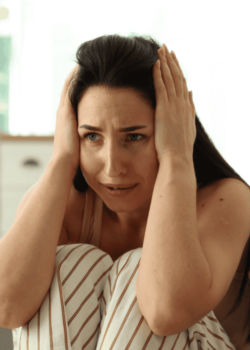 woman sitting in bed with hands on head due to experiencing hypervigilance in adults
