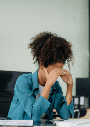 woman at work sitting at desk with head in hands due to overthinking & rumination in adults