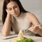 woman sitting at table with meal in front of her looking at food hesitantly due to experiencing loss of appetite in adults