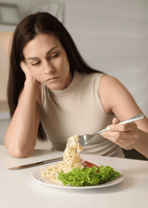 woman sitting at table with meal in front of her looking at food hesitantly due to experiencing loss of appetite in adults