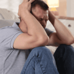 man sat on floor in front of sofa with his hands gripping his head, experiencing panic attacks in adults