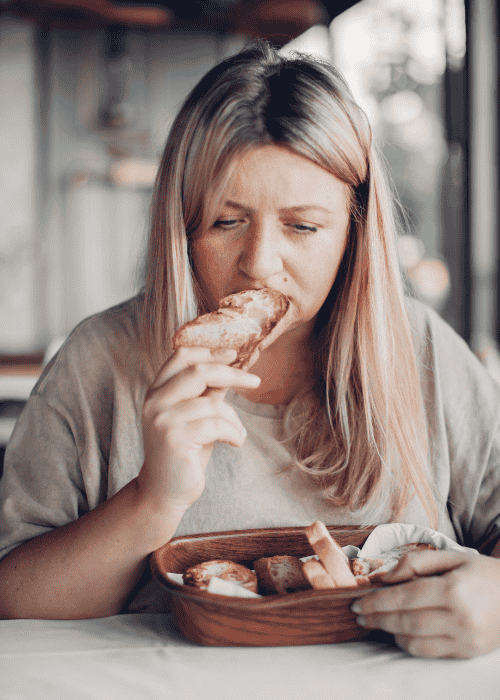 woman sitting at table eating whilst feeling emotional due to stress & emotional eating in adults