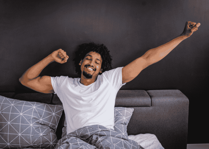 man in bed stretching, smiling after treatment for oversleeping & hypersomnia in adults