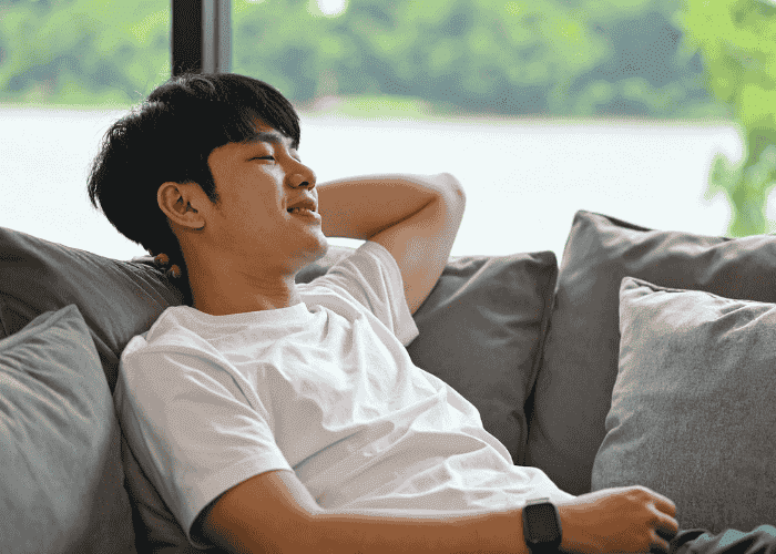 man sitting on a sofa with one arm behind his head relaxing after receiving support for hypervigilance in adults