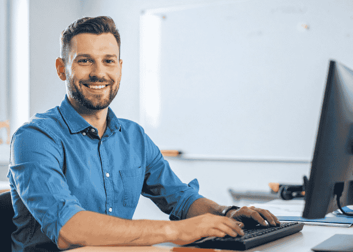 man sitting at desk working on a computer smiling because he is no longer experiencing symptoms of chronic fatigue.