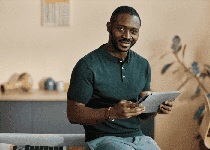 man sitting on desk in office, holding an ipad and smiling confidently after treatment for disorientation and confused thinking in adults.