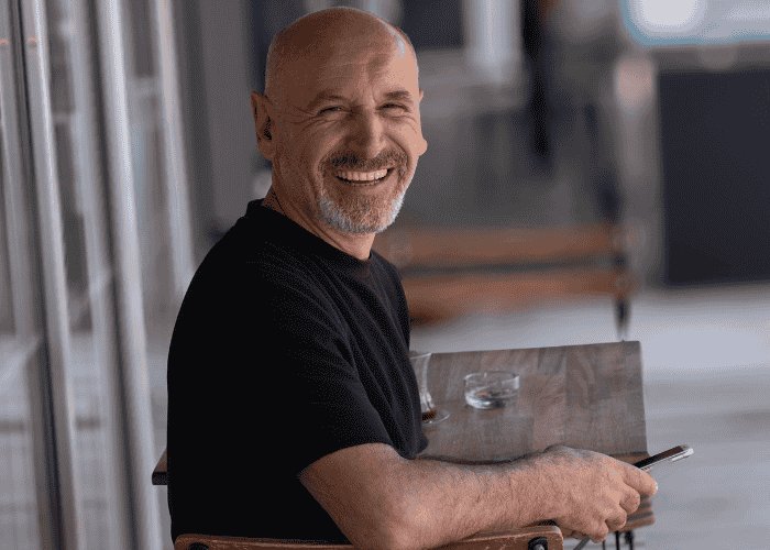man smiling at the camera while sitting outside with his phone in his hand, after recovering from impulsivity in adults