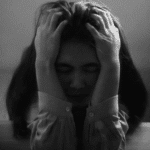 black and white image with a woman with her head in her hands struggling with signs of perfectionism in adults