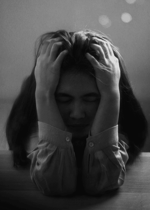 black and white image with a woman with her head in her hands struggling with perfectionism in adults