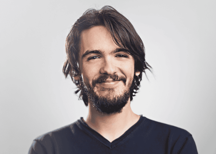 man with a beard and long hair smiling at the camera after overcoming perfectionism in adults