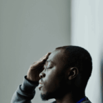 Man with his eyes closed touching his head because he struggles with headaches related to stress & anxiety in adults
