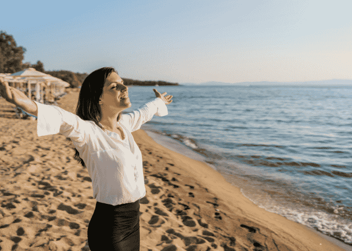 Woman with her arms outstretched looking relieved at the beach after receiving treatment for intrusive thoughts in adults