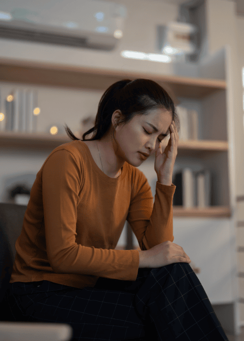 Woman sitting with her hand on her head feeling overwhelmed because of people-pleasing behavior in adults