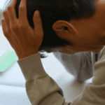 Man sitting with head in hands experiencing thought-related & cognitive symptoms, including indecisiveness