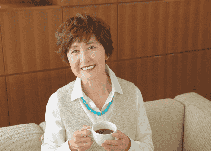 woman smiling drinking cup of coffee on sofa after receiving treatment for crying spells