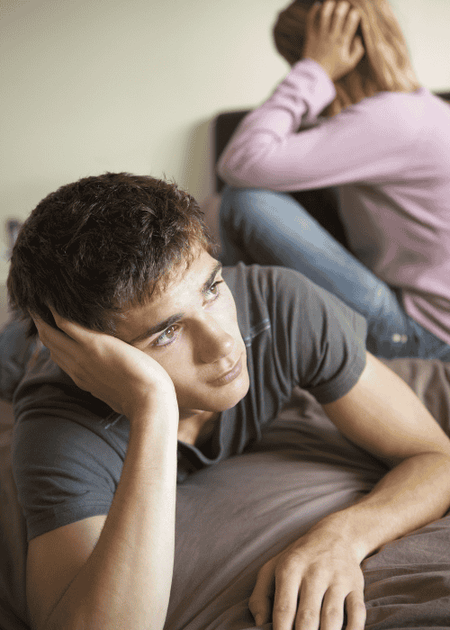 man laying on bed with head in hands with woman in background with her back turned to him due to shifts in sexual desire in adults