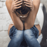 woman sitting on toilet with head in hands due to stress-related urination