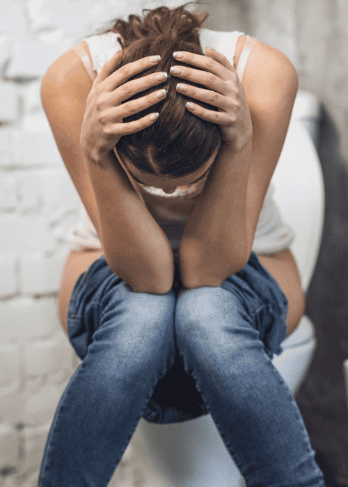 woman sitting on toilet with head in hands due to stress-related urination in adults
