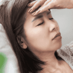 woman sitting on sofa with hand on forehead due to dizziness under stress
