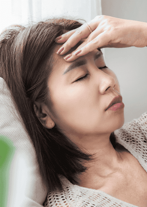 woman sitting on sofa with hand on forehead due to dizziness under stress in adults