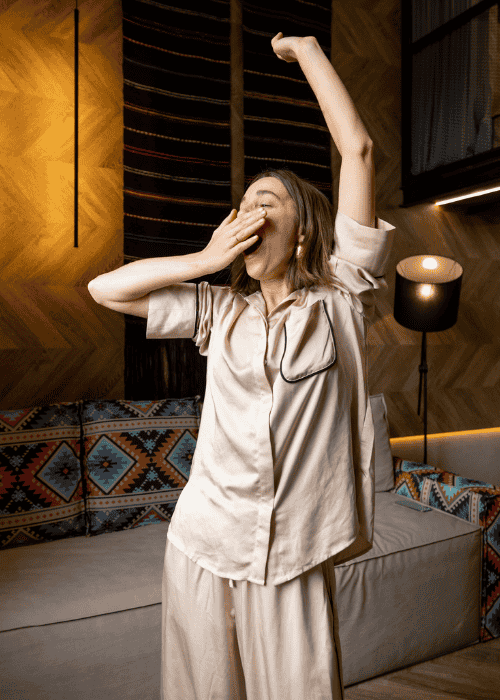 tired woman in bedroom in pyjamas yawning and stretching after experiencing parasomnias in adults