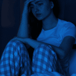 woman awake in bed at night sitting up with head in hand due to nighttime anxiety in adults