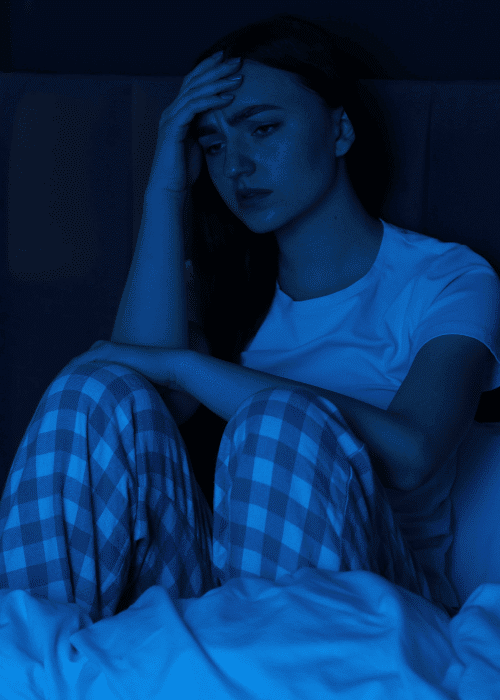 woman awake in bed at night sitting up with head in hand due to nighttime anxiety in adults