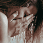 woman crying with hands over face and hair falling forwards experiencing trauma- related emotional flashbacks