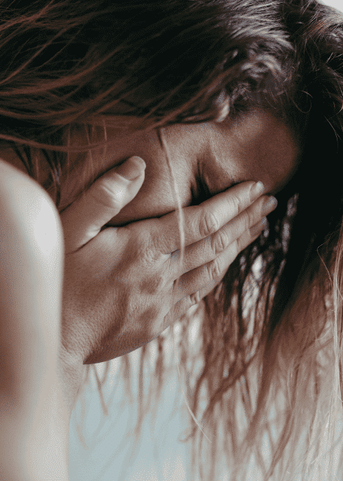 woman crying with hands over face and hair falling forwards experiencing trauma- related emotional flashbacks