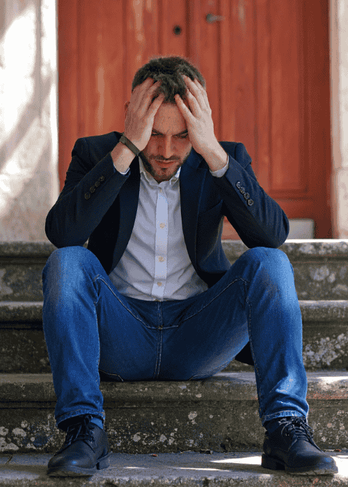 man sitting outside on step in front of door with head in hands due to compromised judgment under stress.