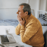 man sitting with face in hands at desk in home office looking confused due to false memories in adults