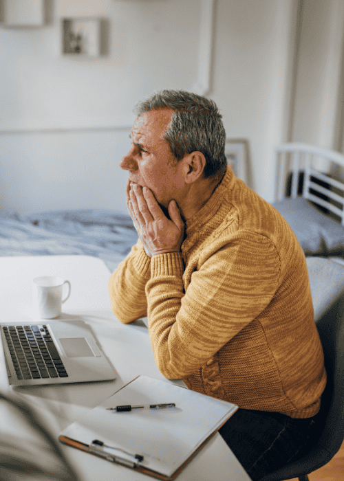 man sitting with face in hands at desk in home office looking confused due to false memories in adults
