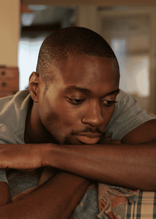 A man leaning on the back of a sofa with his arms crossed and his chin resting on his forearms experiencing chronic dissatisfaction