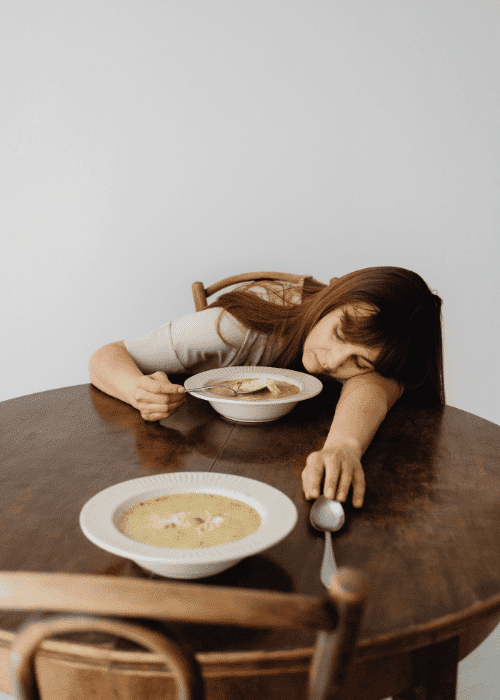 Woman asleep at the table during lunchtime, struggling with daytime fatigue & low energy in adults