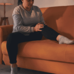 Woman sitting on the couch looking at her leg due to paresthesia related to stress