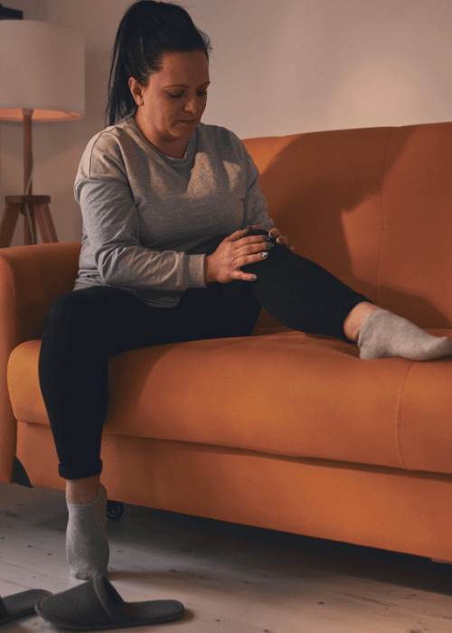 Woman sitting on the couch looking at her leg due to paresthesia related to stress