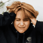 Woman with her face scrunched up and her hands clutching her head due to interruptions in thought processes in adults